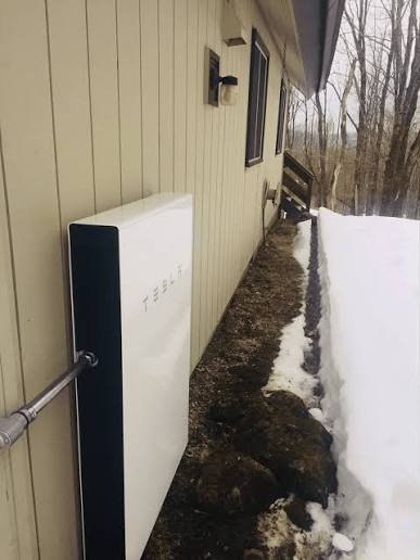 Tesla Powerwall installed on the side of a house in snow.